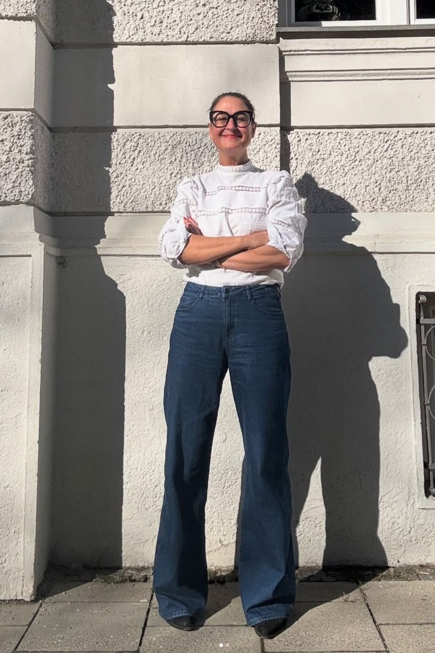 Mirjam Smend steht selbstbewusst vor einer hellen Fassade und blickt in die Kamera